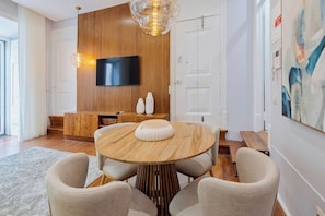 A modern living room with a round wooden table, two chairs, a flat-screen TV mounted on a wooden wall, and a painting on the wall. - Live In Setúbal III (Setúbal)