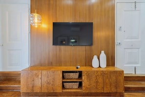 A wooden reception desk with a flat-screen TV, two white vases, and woven baskets. - Live In Setúbal III (Setúbal)