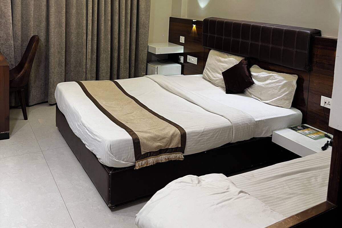 Quarto de hotel com cama, cadeira, escrivaninha, ventoinha no teto e mesa de cabeceira.