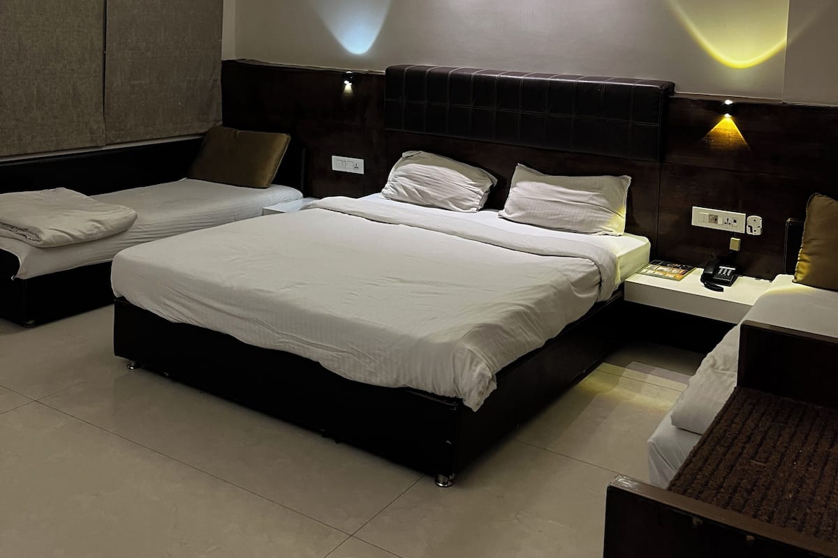 Quarto de hotel com uma cama grande, duas camas menores, um ventilador de teto, abajures e uma mesa de cabeceira com telefone.