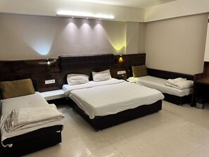 Ein Hotelzimmer mit einem großen Bett, einem kleineren Bett, einem Schreibtisch und einem Mülleimer.
