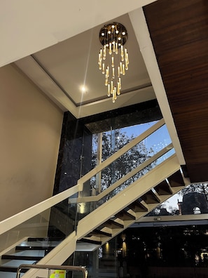 Ein modernes Interieur mit einer Treppe, einer Kandelaberleuchte und großen Fenstern.