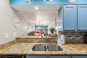 A kitchen with granite countertops, a double sink, blue cabinets, and a decorative starfish wall art piece. - Charming 2-bedroom townhouse in Panama City Beach, perfect for families! (Panama City Beach)