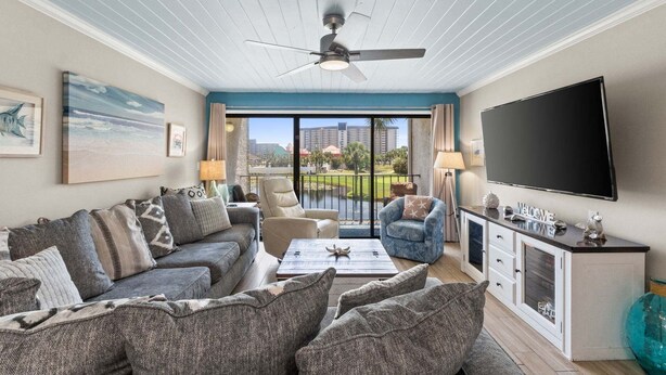 Ein Wohnzimmer mit einer Couch, Sesseln, einem Couchtisch, einem Fernseher und einem Balkon mit Blick.