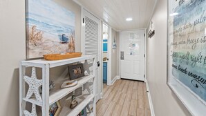 Ein Flur mit einem Strandgemälde, einem weißen Konsolentisch mit Dekoration und einer Tür zu einem Zimmer.