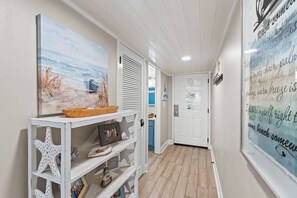 A hallway with a beach-themed painting, a white console table with decorative items, and a door leading to a room. - Charming 2-bedroom townhouse in Panama City Beach, perfect for families! (Panama City Beach)