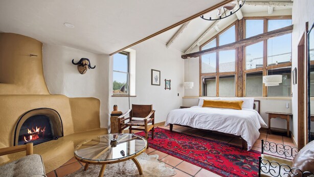 Una habitación con chimenea, una cama, un sofá, una mesa de vidrio y una alfombra roja estampada.