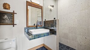 Un baño con lavamanos blanco, espejo y zona de ducha.