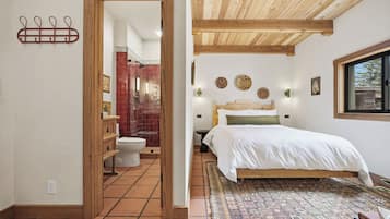 Un dormitorio con techo de madera, alfombra estampada, cama con ropa de cama blanca y ventana con vistas.