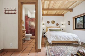 A bedroom with a wooden ceiling, a patterned rug, a bed with white bedding, and a window with a view. - Hey House (Buena Vista)