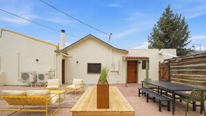 Un patio con una mesa y bancos de madera, un sofá amarillo y una planta en maceta.