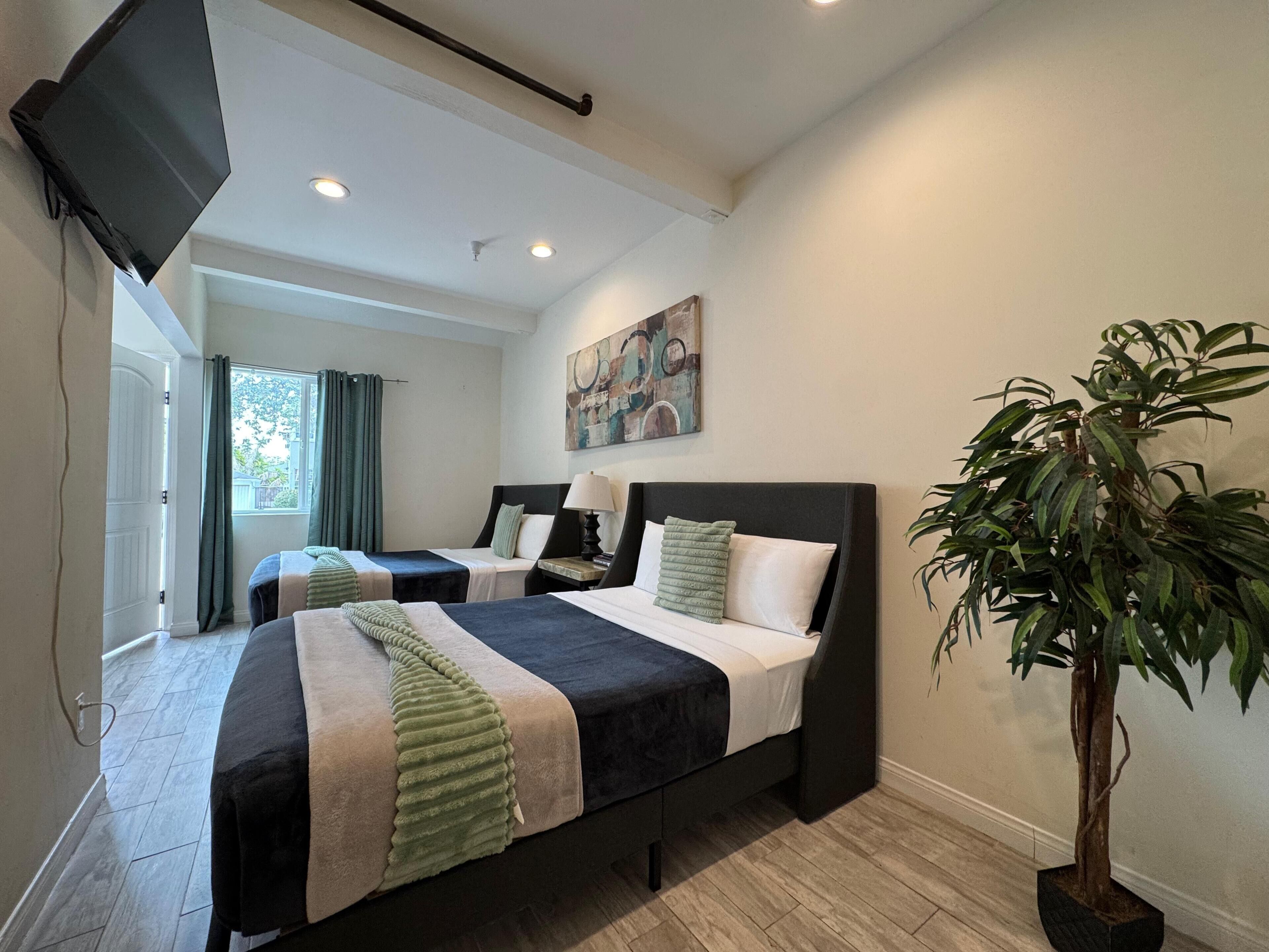 A hotel room with two beds, a flat-screen TV, a painting, and a potted plant.