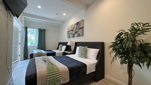 Une chambre d’hôtel avec deux lits, un téléviseur à écran plat, un tableau et une plante en pot.