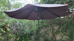 Une table ronde d’extérieur, surmontée d’un grand parasol, et entourée de six chaises aux motifs complexes.