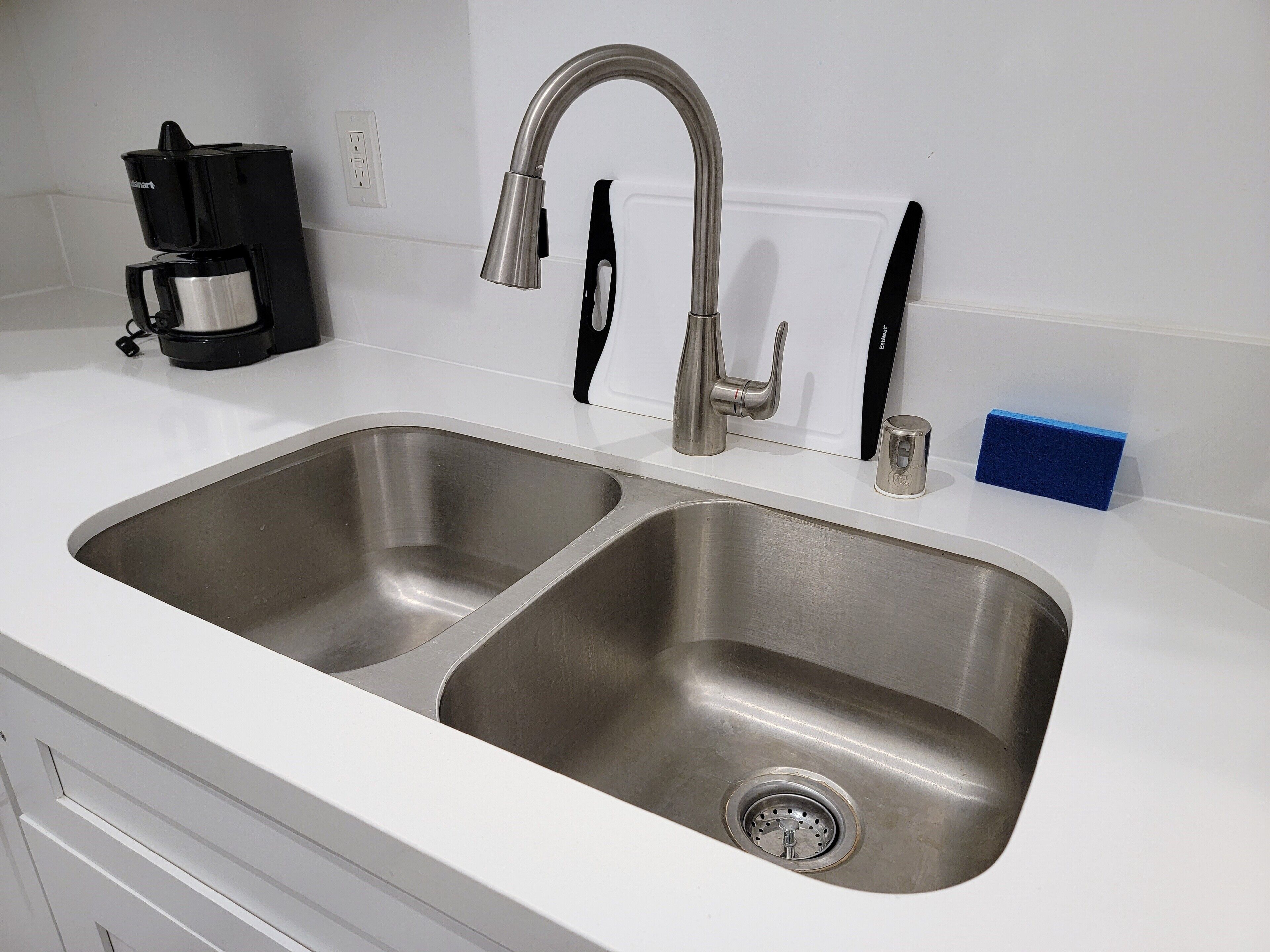 A kitchen with two stainless steel sinks, a coffee maker, and a sponge holder.