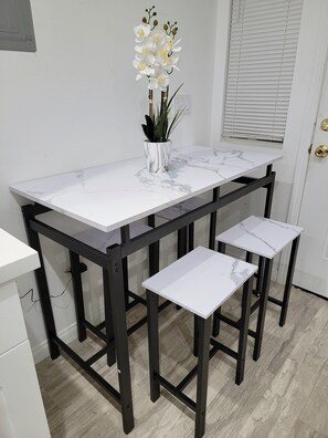 Une table en marbre blanc avec des pieds en métal noir, un vase blanc rempli de fleurs et une porte blanche dotée d’une fenêtre.