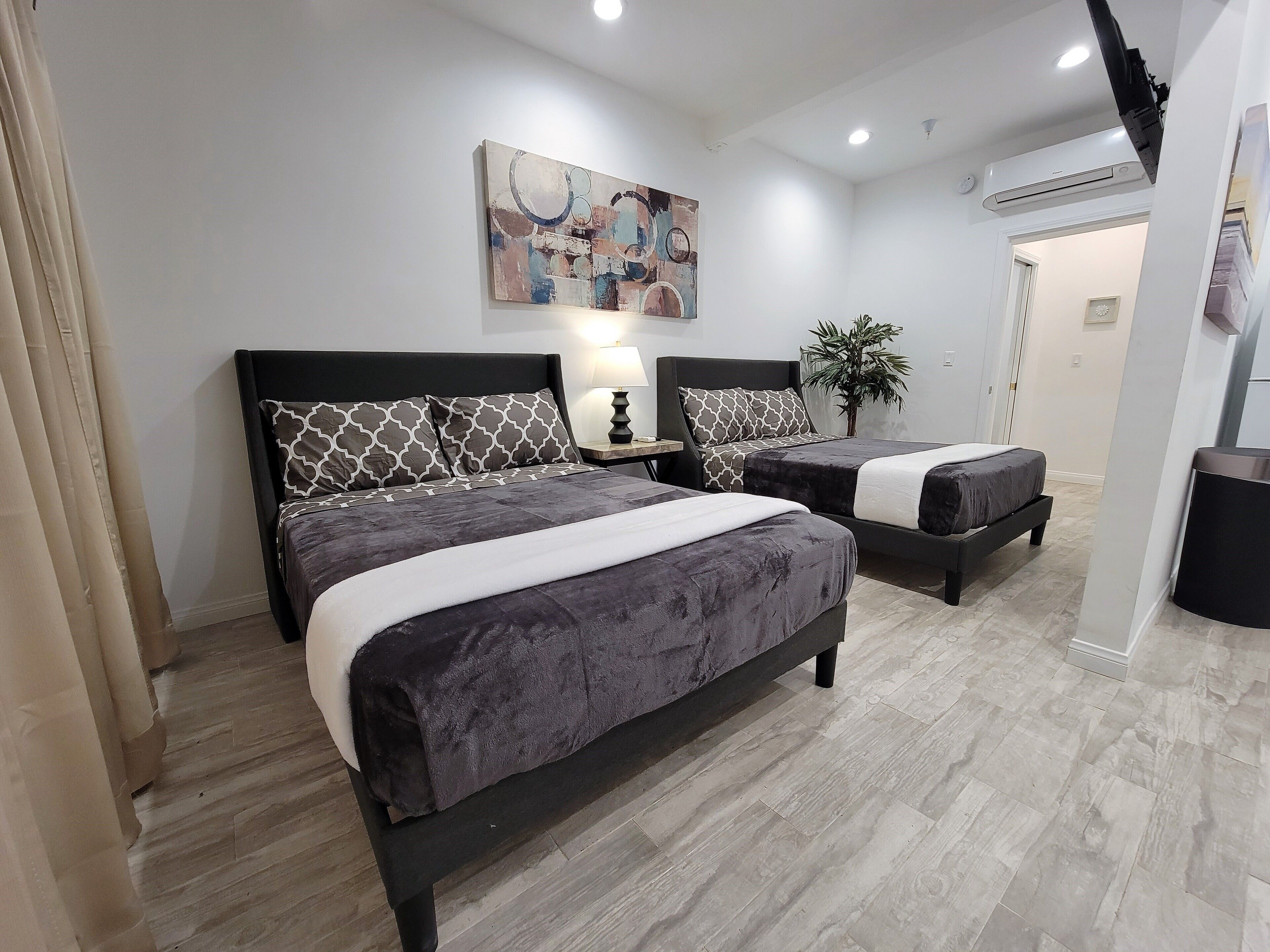 Un dormitorio moderno con dos camas, un cuadro, una mesita de noche, una lámpara y un equipo de aire acondicionado.