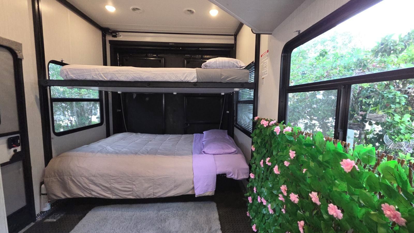 A bunk bed room with a window, a small rug, and a green plant with pink flowers.