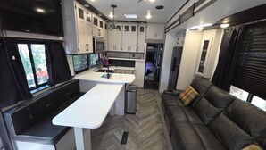 An RV interior with a kitchenette, a dining area, and a seating area with a sofa.
