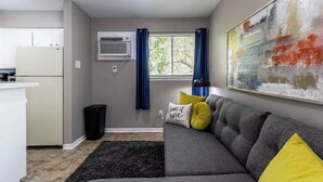 Een woonkamer met een grijze bank, een zwart tapijt, een raam met blauwe gordijnen en een schilderij aan de muur.