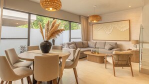 En moderne stue med sofa, spisebord, stole og et stort vindue.