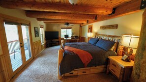 Ein Schlafzimmer mit einem Bett, einem Schreibtisch mit Computer, einem Fernseher und einer Holzbalkendecke.