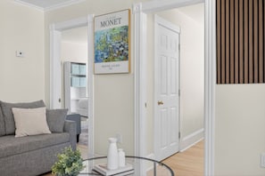 Un salon avec un canapé gris, une table basse en verre, un vase blanc et un tableau encadré représentant les « Nymphéas » de Monet.