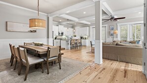 A spacious living area with a dining table, chairs, a sofa, and a kitchen in the background. - A Wavy Days | 5BR 30A | Steps to Pool | Sleeps 12 | Golf Cart + Bikes (Santa Rosa Beach)