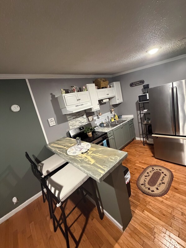 A compact kitchen with a dining table, chairs, a refrigerator, and a microwave.