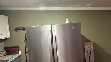 Un frigorifero in acciaio inox in una cucina con piano di lavoro in legno, un cartello con su scritto 'Cercasi aiuto in cucina' e un cartello di benvenuto sul muro.