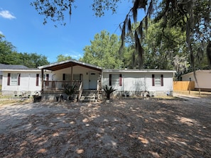 A mobile home with a porch, air conditioning units, and a fenced yard.