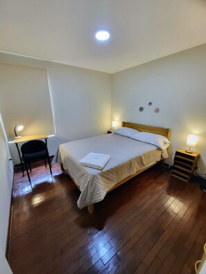 A bedroom with a bed, bedside lamps, a desk with a chair, and a small shelf. - Apartment 3 Bedrooms | 1 block from Larcomar and Marriott (Miraflores)