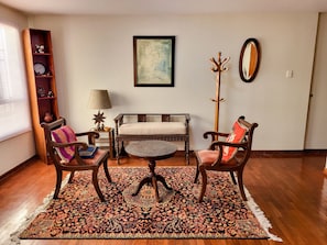 A living room with a sofa, two armchairs, a coffee table, a floor lamp, a side table with a lamp, a bookshelf, and a framed picture on the wall. - Apartment 3 Bedrooms | 1 block from Larcomar and Marriott (Miraflores)
