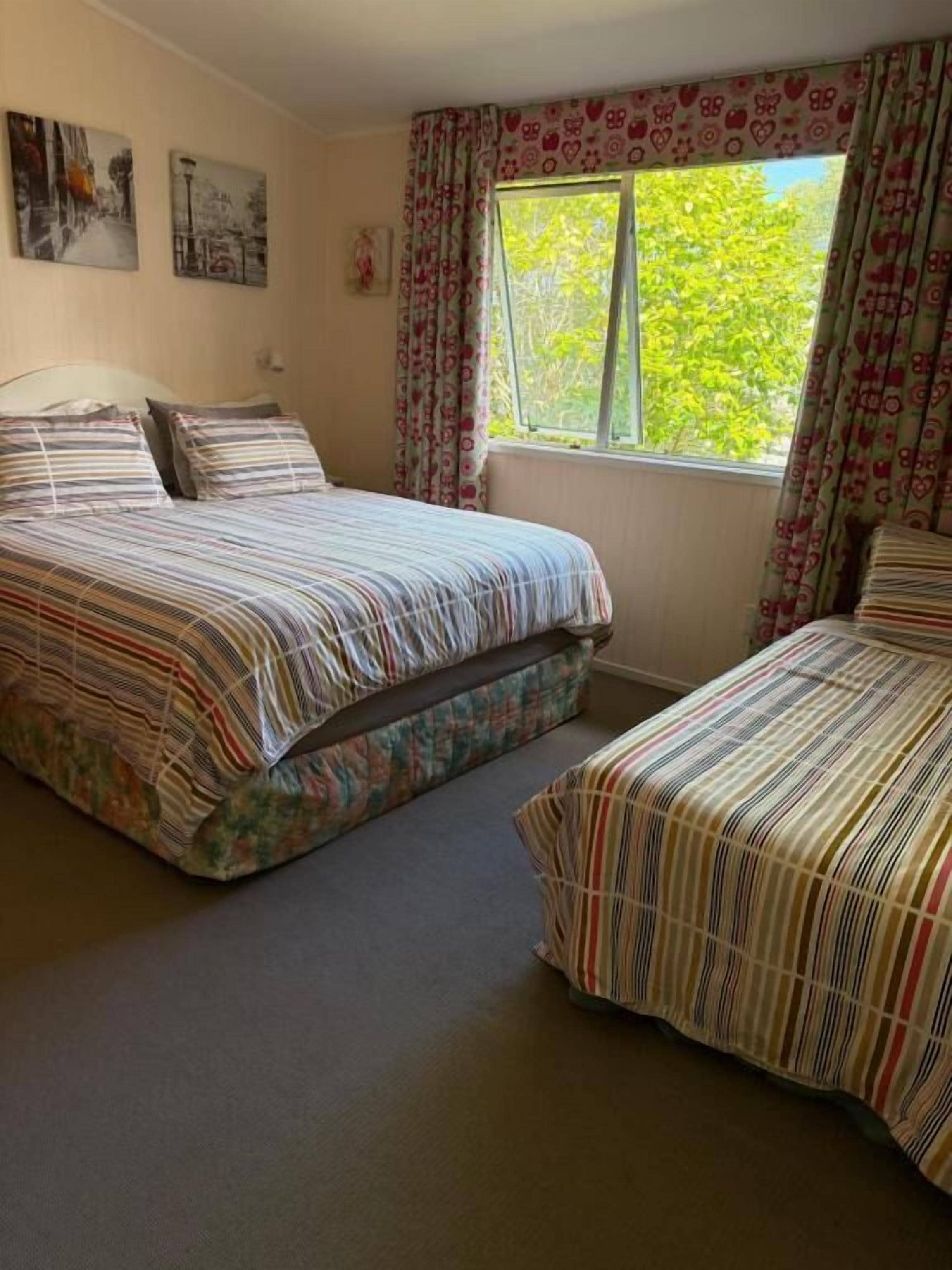 Une chambre avec deux lits, une fenêtre avec des rideaux et des œuvres d’art murales.