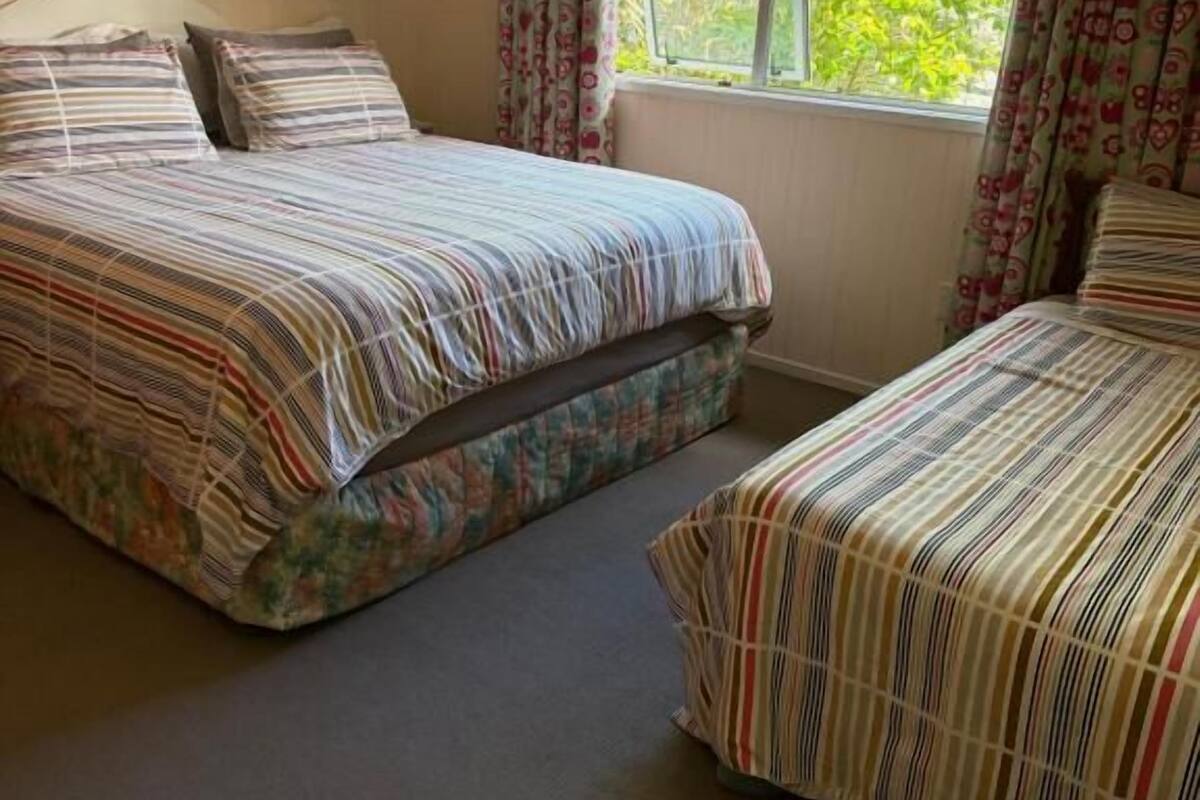 A bedroom with two beds, a window with curtains, and wall art.
