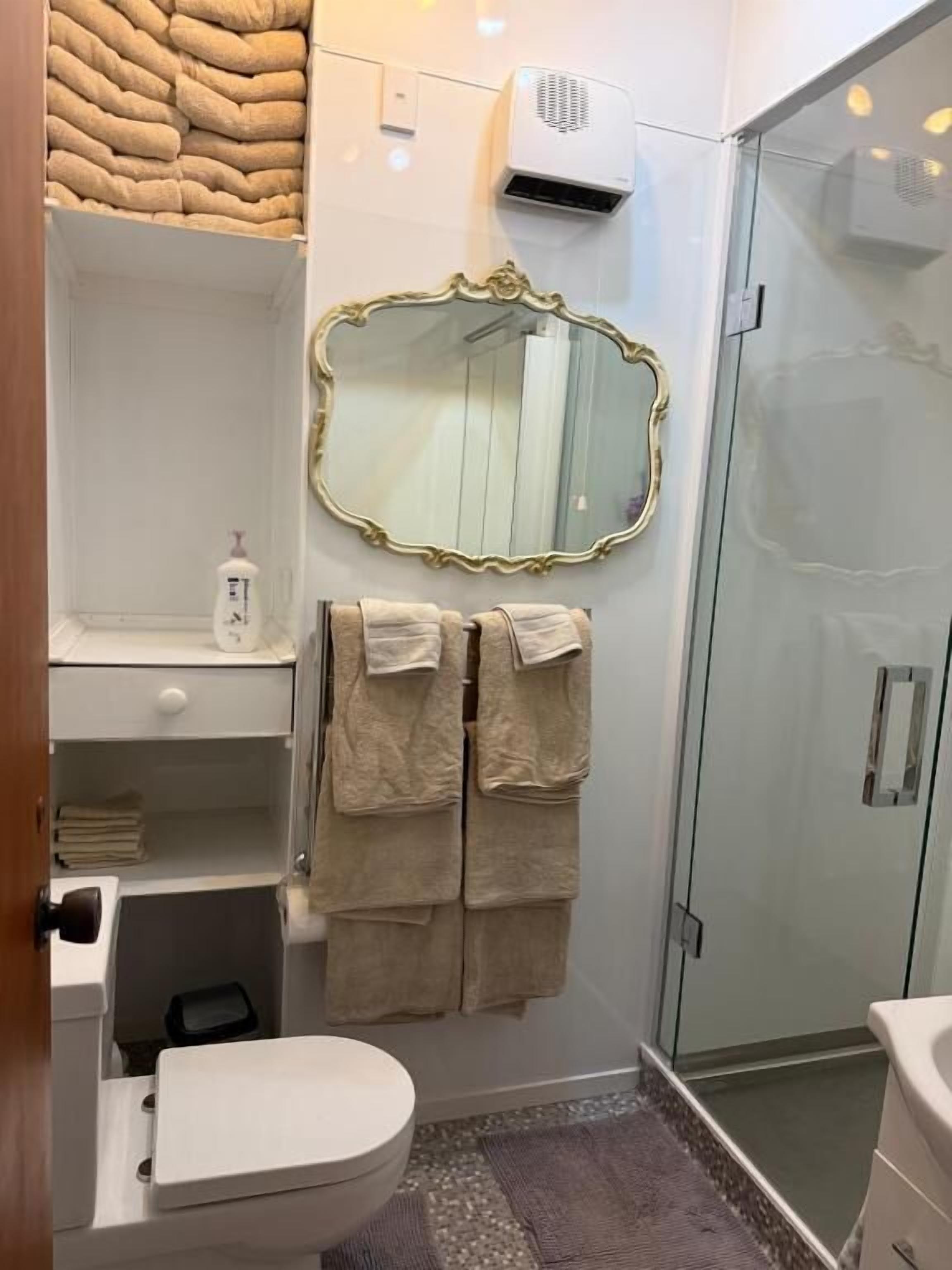 A bathroom with a glass shower enclosure, a white toilet, a sink with a mirror, and a towel rack.