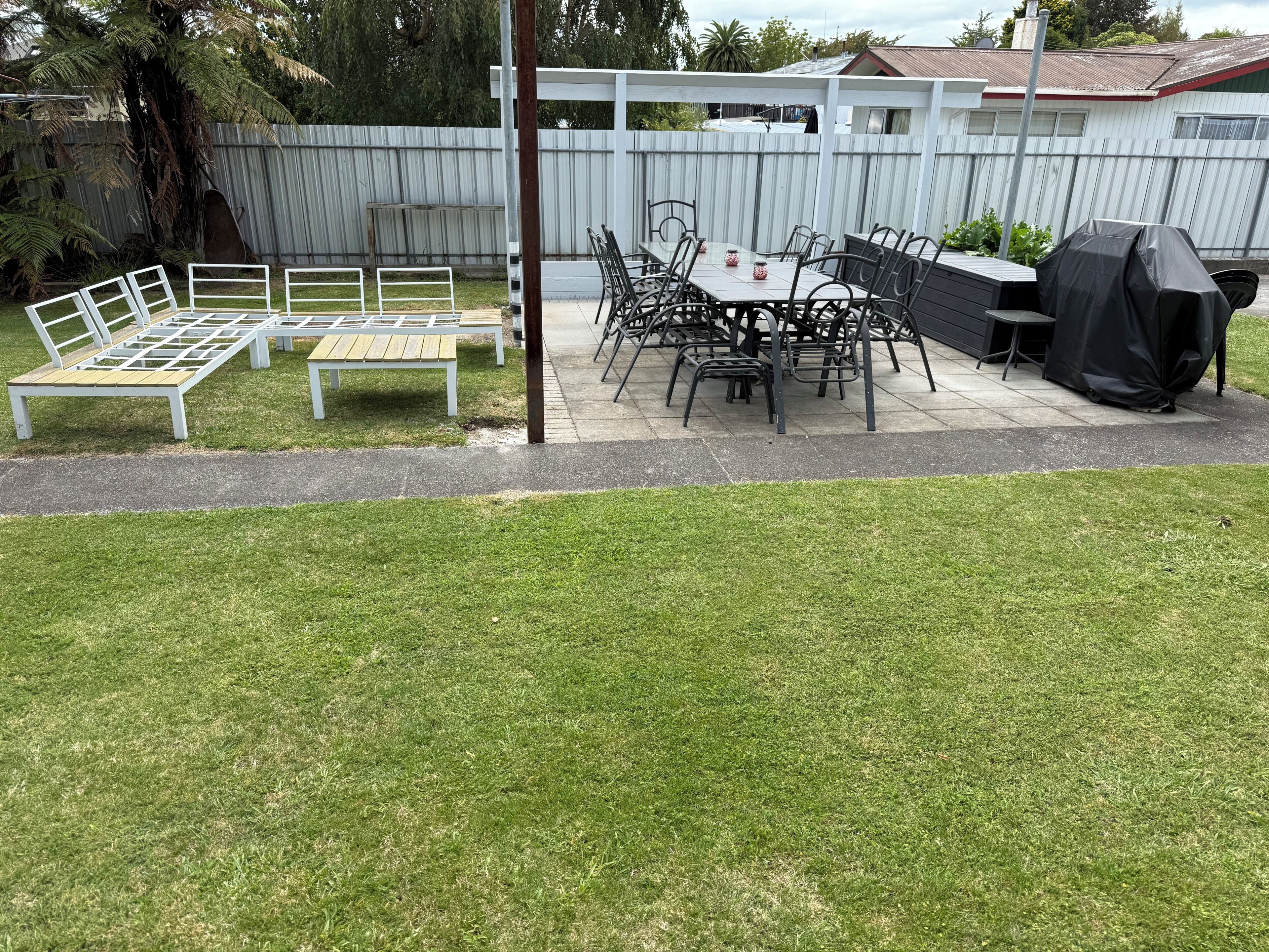 A patio with a table and chairs, a barbecue grill, and a white fence.