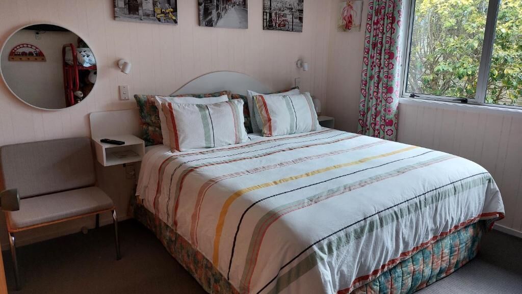 Une chambre à coucher avec un lit, une table de chevet, une chaise, un miroir et une fenêtre avec des rideaux.