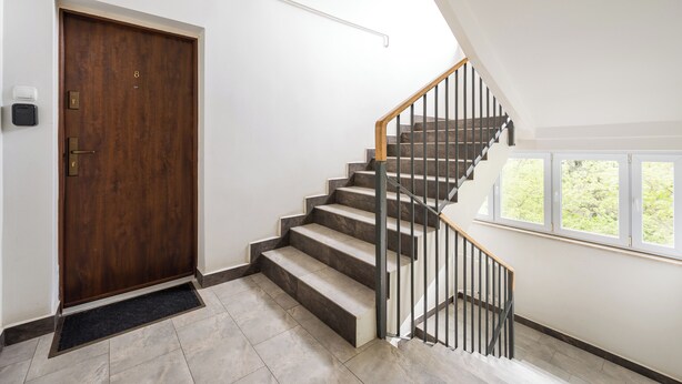 A staircase with a wooden handrail and a black metal railing, leading to a landing with a door. - Royal Baths Spacious Apartment (Warszawa)