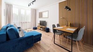 A modern living room with a blue sofa, a wooden dining table, and a TV.