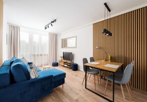 Una sala de estar moderna con un sofá azul, una mesa de comedor de madera y un televisor.