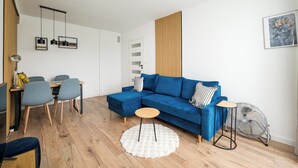A modern living room with a blue sectional sofa, a round coffee table, and a dining area with a table and chairs.