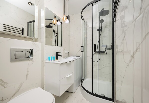 A modern bathroom with a glass-enclosed shower, a white vanity, and a marble backsplash.