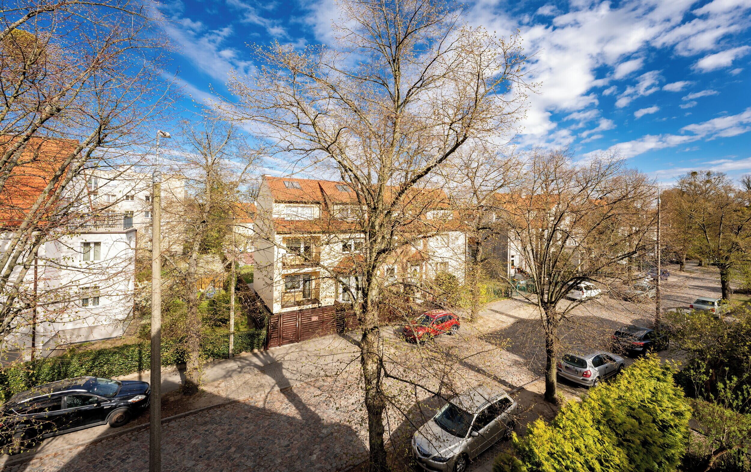 Ett bostadsområde med parkerade bilar, träd och byggnader med rödfärgade takpannor.