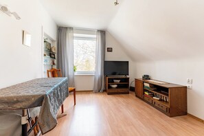 Una habitación con una mesa, un televisor, una estantería y un ventanal con cortinas.