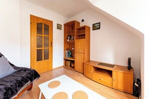 Una habitación con un armario de madera, una mesa blanca con detalles circulares, un sofá de color oscuro y una puerta de madera con paneles de vidrio.
