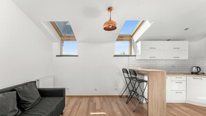 Et moderne køkken med ovenlysvinduer, et spiseområde med et træbord og stole, samt en mørk sofa.