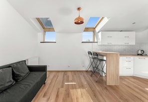 Eine moderne Küche mit Oberlichtern, ein Essbereich mit Holztisch und -stühlen sowie ein dunkelgraues Sofa.