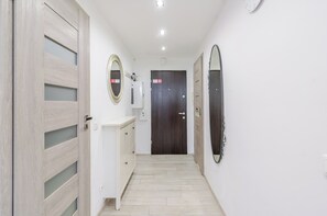 A hallway with a wooden door, a white wall, a mirror, and a dark door at the end.