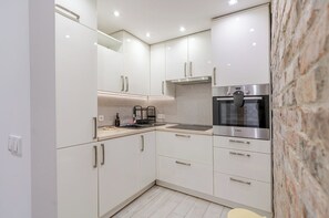 A modern kitchen with white cabinets, a Bosch oven, and a stone wall.